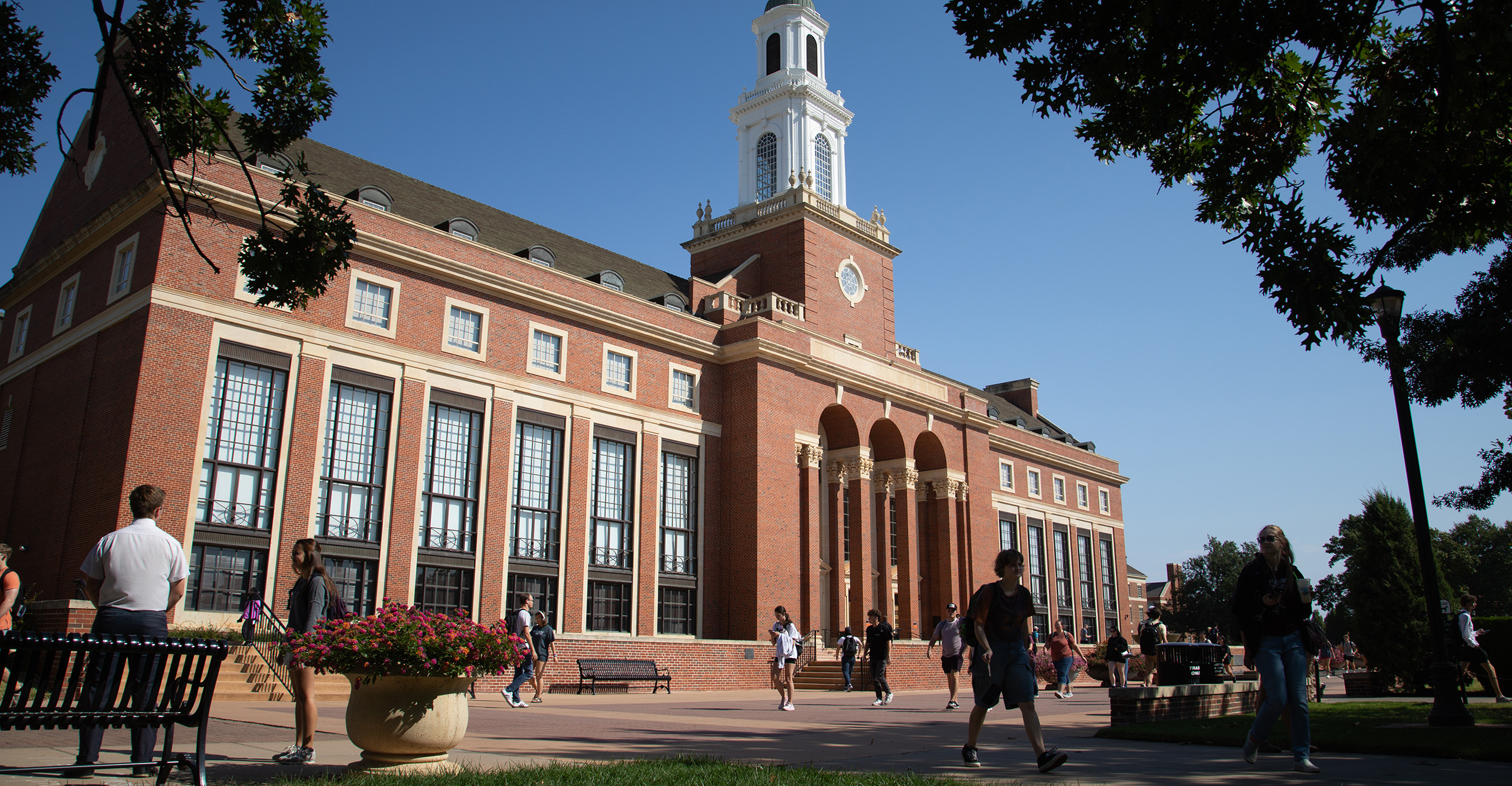 Exterior view of Oklahoma State University’s Edmon Low Library with its clock tower and columns, as people walk and gather on the surrounding campus lawn.