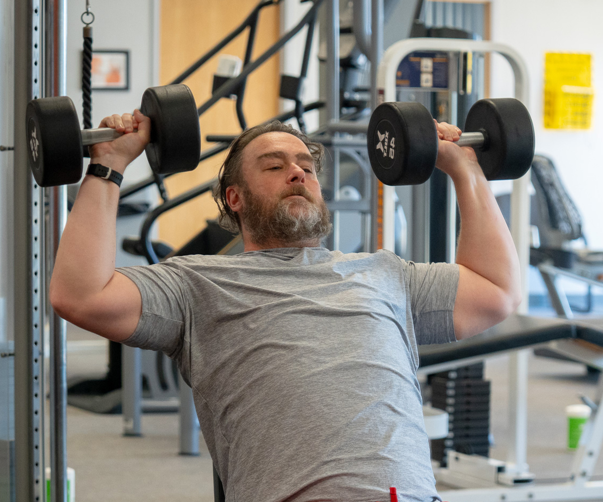 Shot of Greg Van Ness working out with dumbbell weights while inclined on a bench.