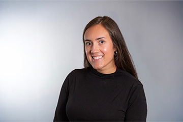 Portrait of a smiling woman with long brown hair wearing a black top against a light gray background.