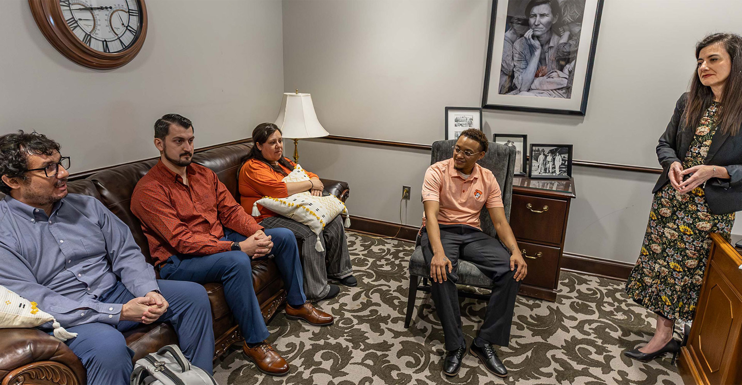 A group of people have a discussion while gathered around a room.