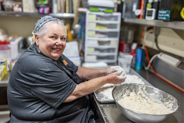 Cowboy Café staff member kneading fry bread dough by hand at a stainless steel prep station, smiling at the camera.