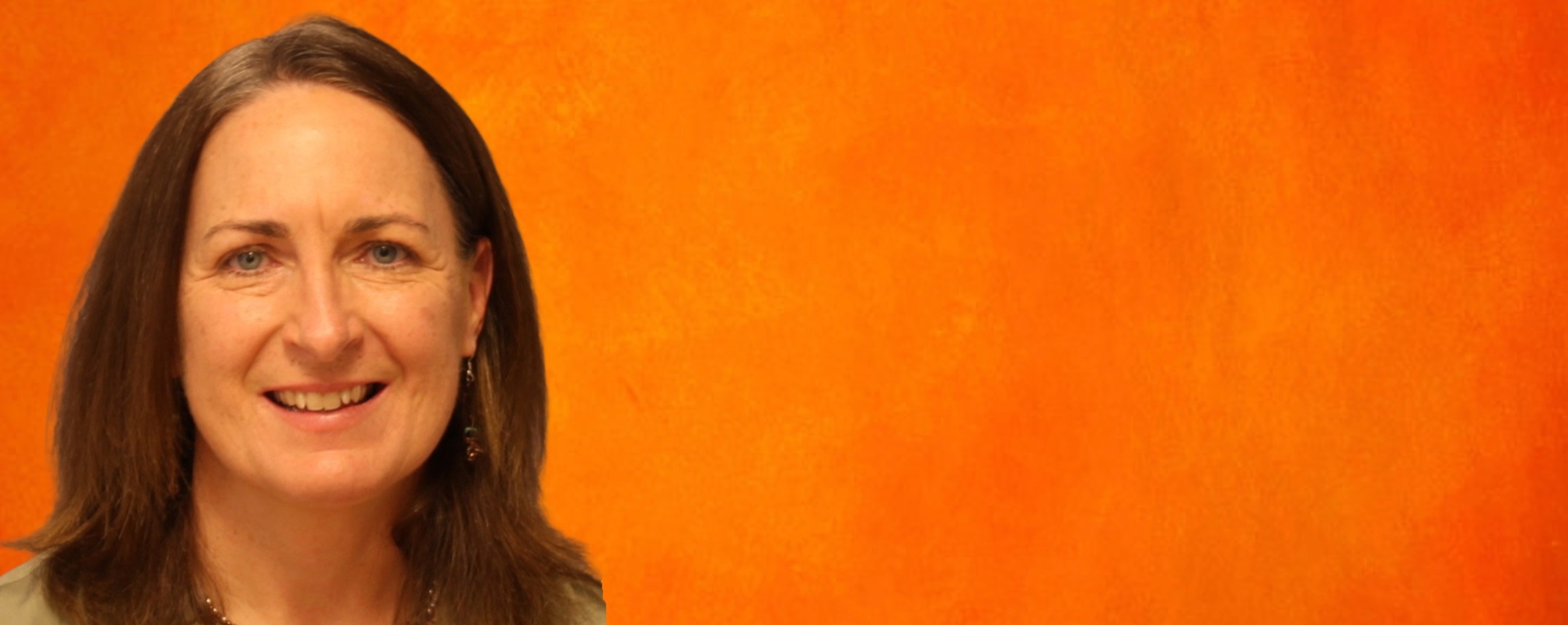 OSUIT Communications instructor Amy Reynolds smiles in front of an orange background.