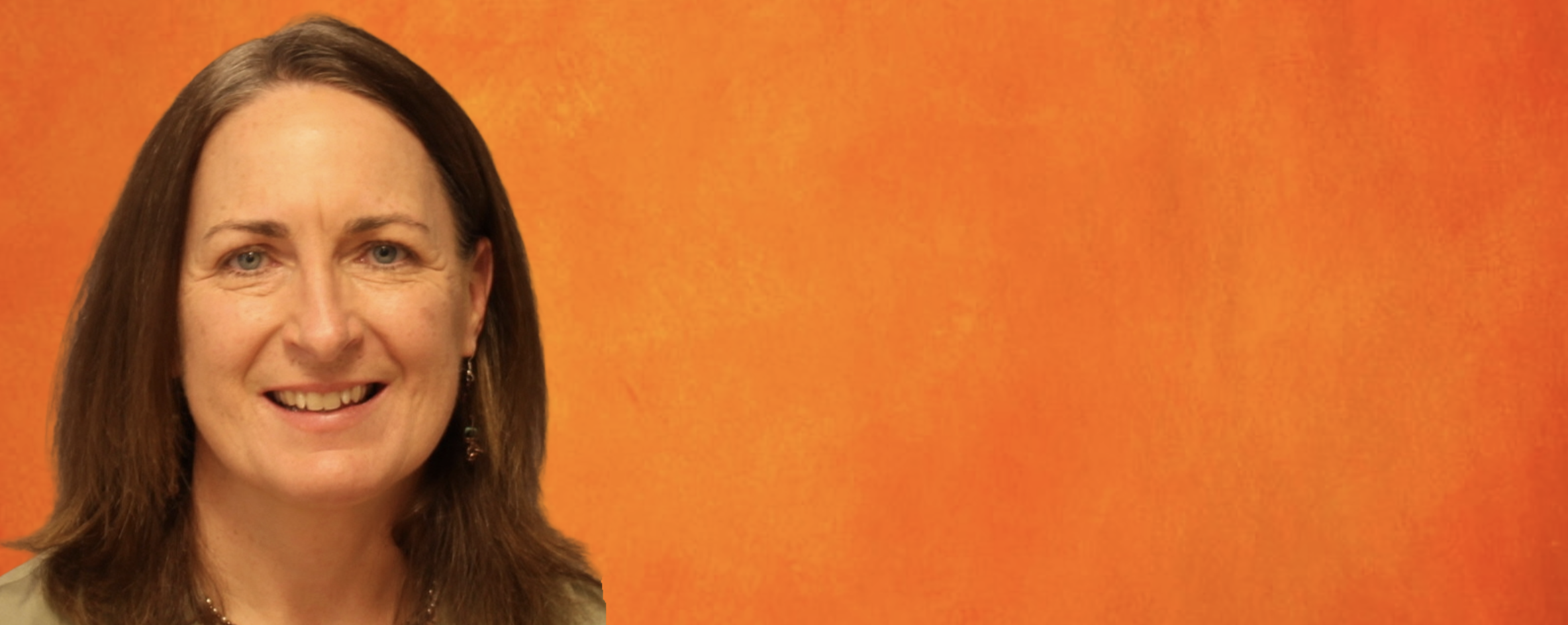 Portrait-style image of a person with shoulder-length brown hair against a textured orange background, framed from the shoulders up for a professional or profile-style photograph