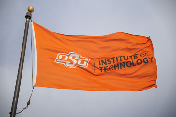 An orange OSUIT flag is waving on a flag pole.