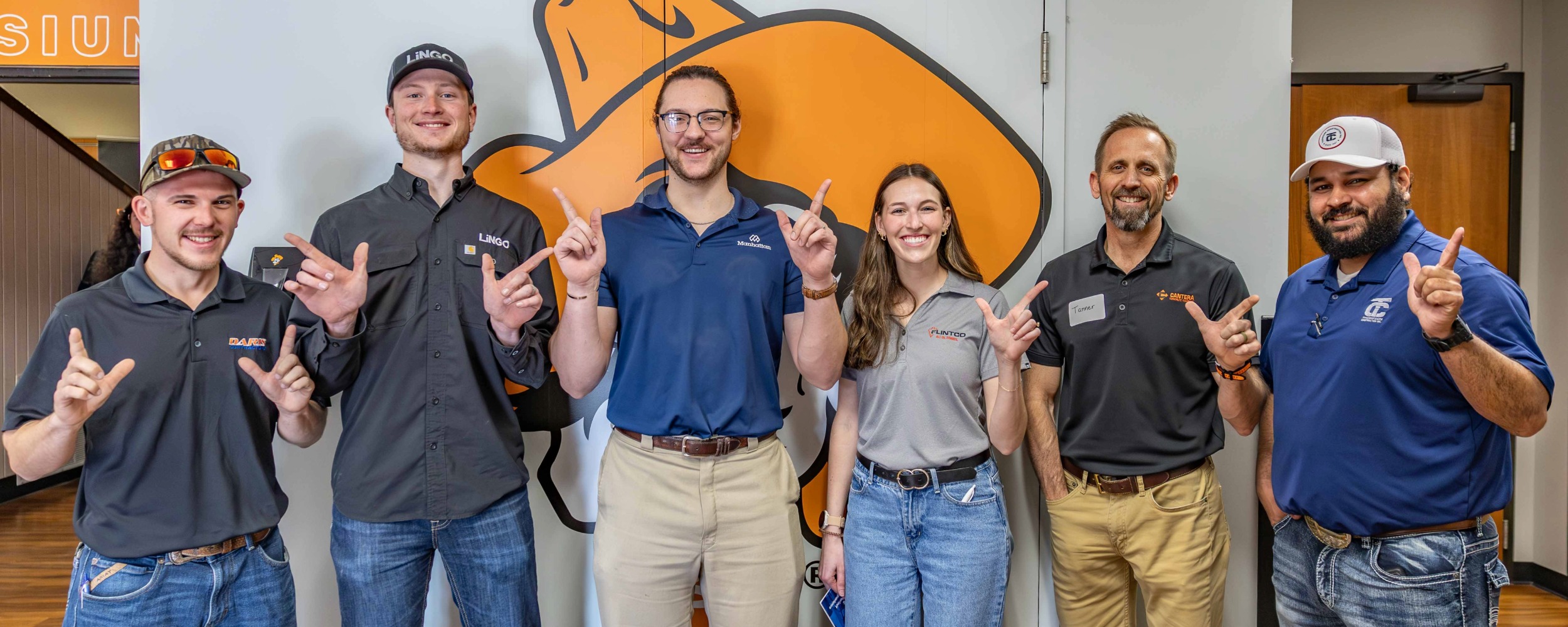Six OSUIT alumni pose in front of an OSU Institute of Technology branded wall featuring the Pistol Pete logo, all holding up the "Go Pokes" hand sign. The group represented various employers at the Spring 2026 Career Fair.