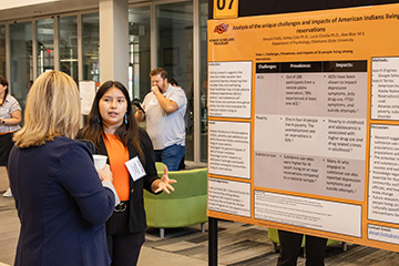 A researcher discusses a poster presentation about pain research with an attendee, reflecting the research foundation behind efforts to address chronic pain disparities in Native American communities.