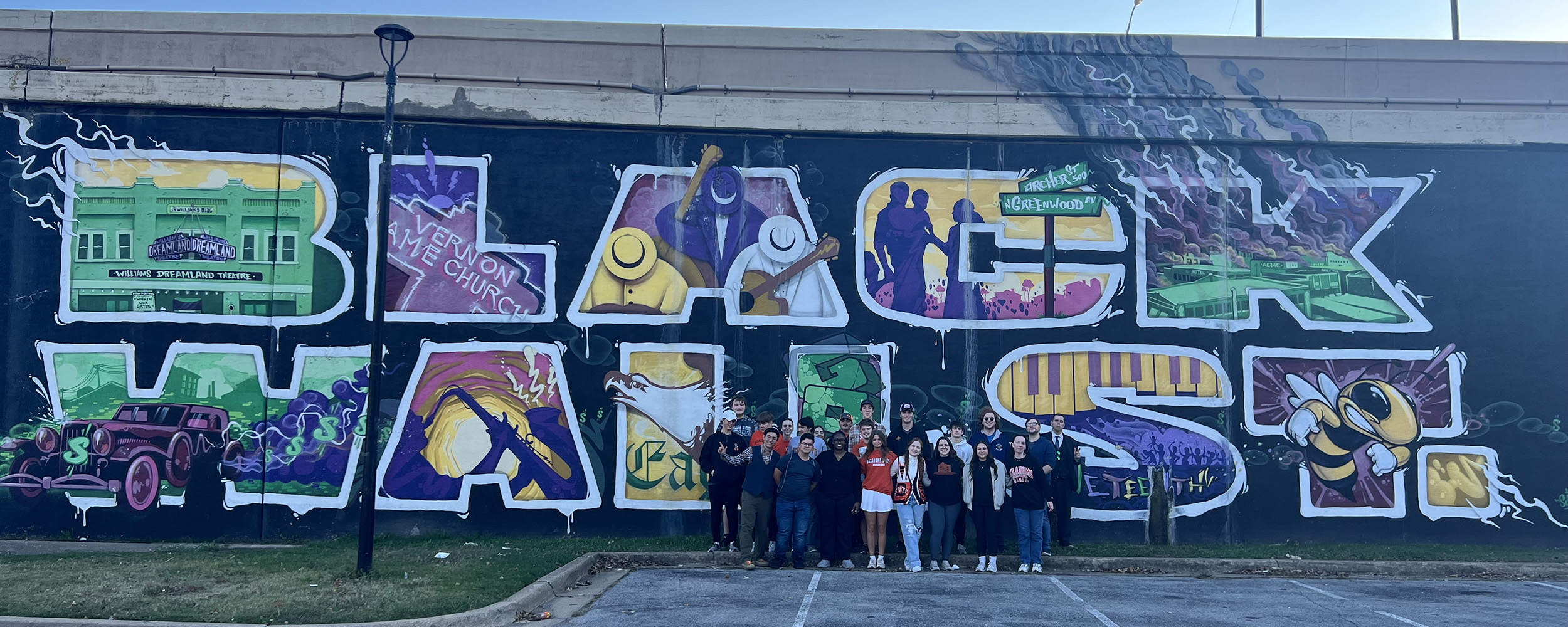 Students of the honors Black Wall Street History course line up in front of the I-244 Black Wall Street mural on Greenwood Avenue for a photo.
