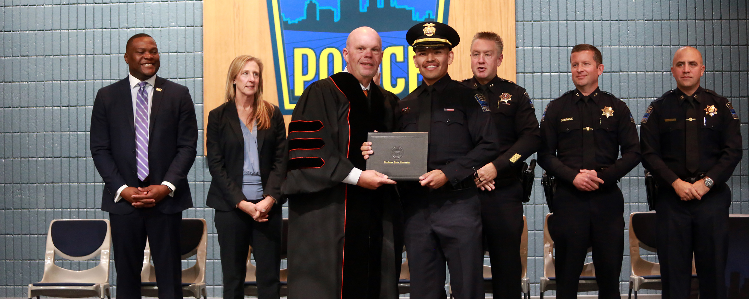 OSU-Tulsa Interim President Johnny Stephens (Center Left) poses with newly graduated Officer Brenden Olguin (Center Right) in front of a line of city officials at the ceremony.