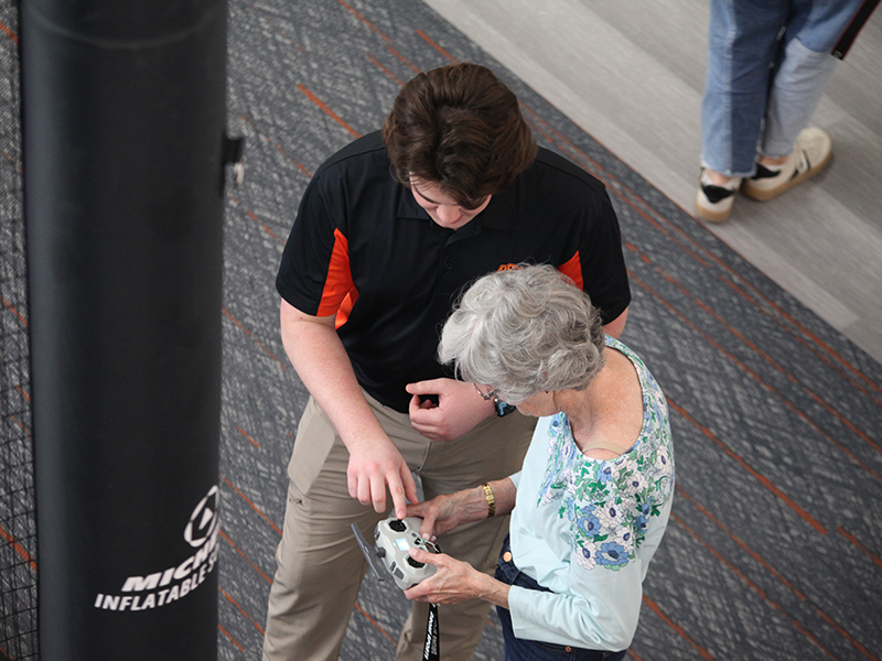 An OSU student helps a woman with the controls of a drone soccer drone.