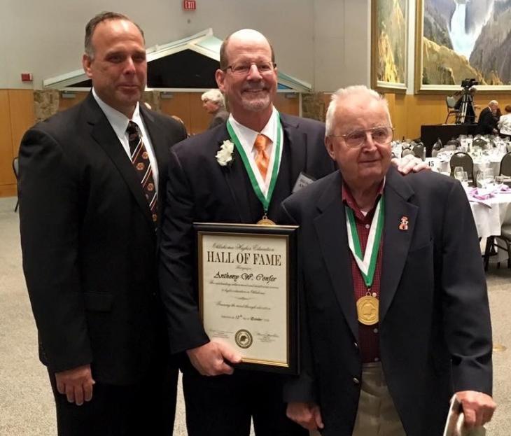 Three Caucasian men pose with a frame with a document that says Hall of Fame.
