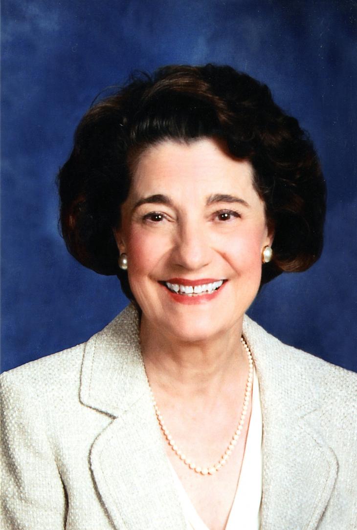 A Caucasian woman with curly black hair and a white blouse poses.