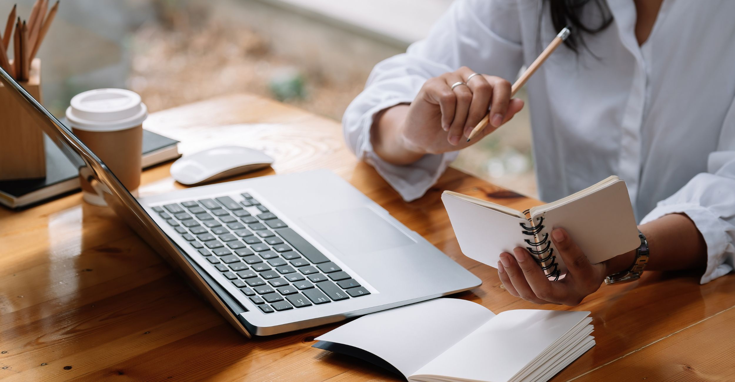 stock image of person holding pencil and notebook looking at a laptop screen