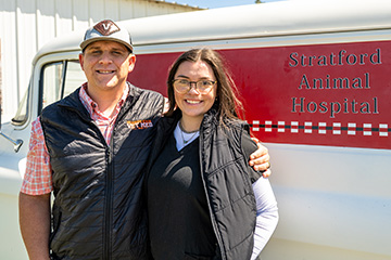 Two individuals wearing black OSU Veterinary Medicine vests stand side by side smiling in front of a vehicle labeled “Stratford Animal Hospital,” posing for a portrait outdoors.
