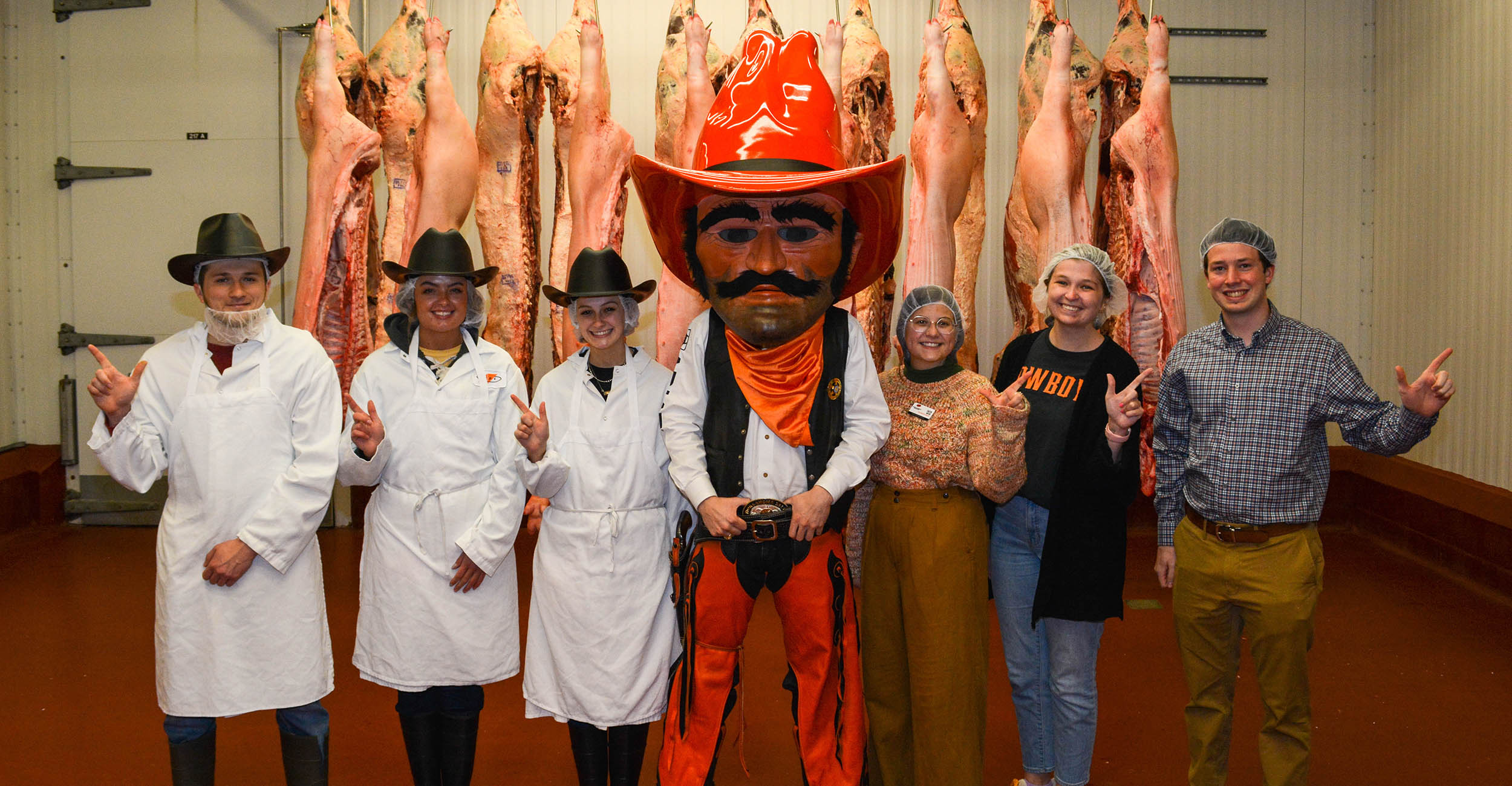 Students and volunteers standing in front of livestock carcasses in the meat processing facility at OSU.