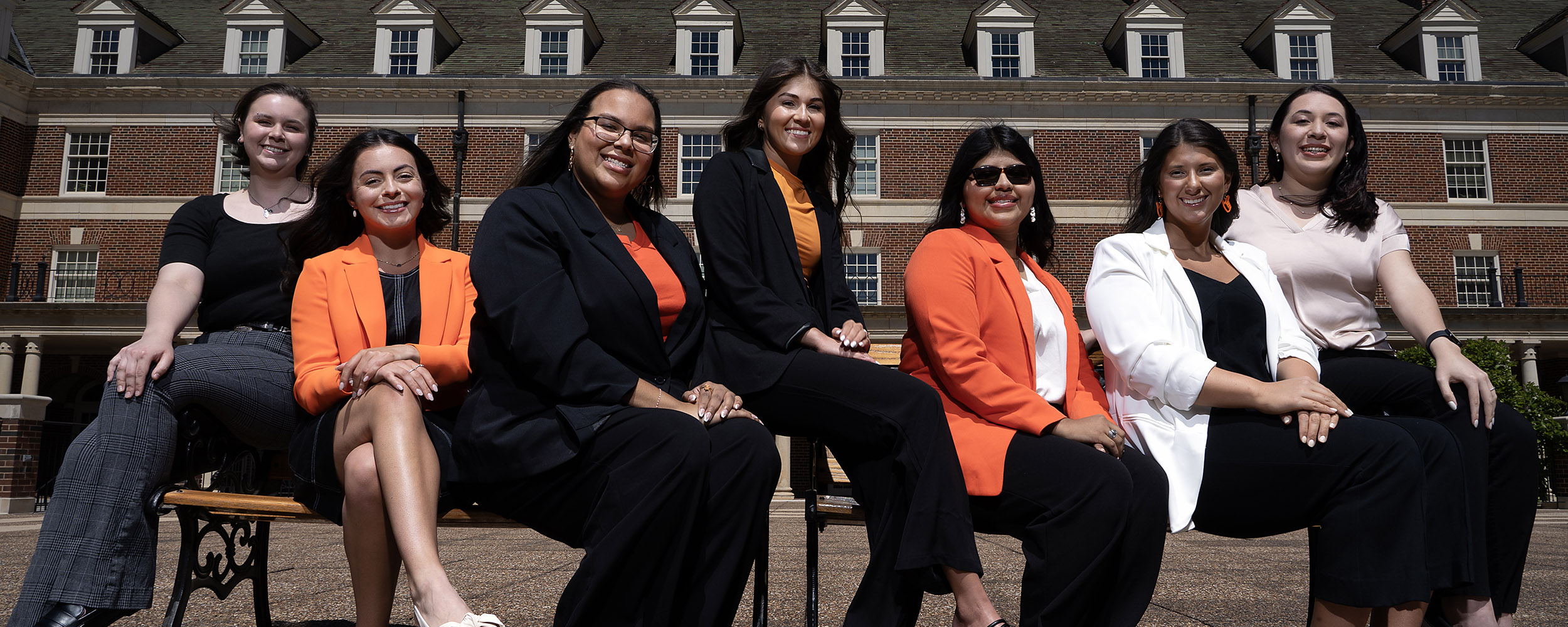 Seven women sit on a bench outside Willard Hall.