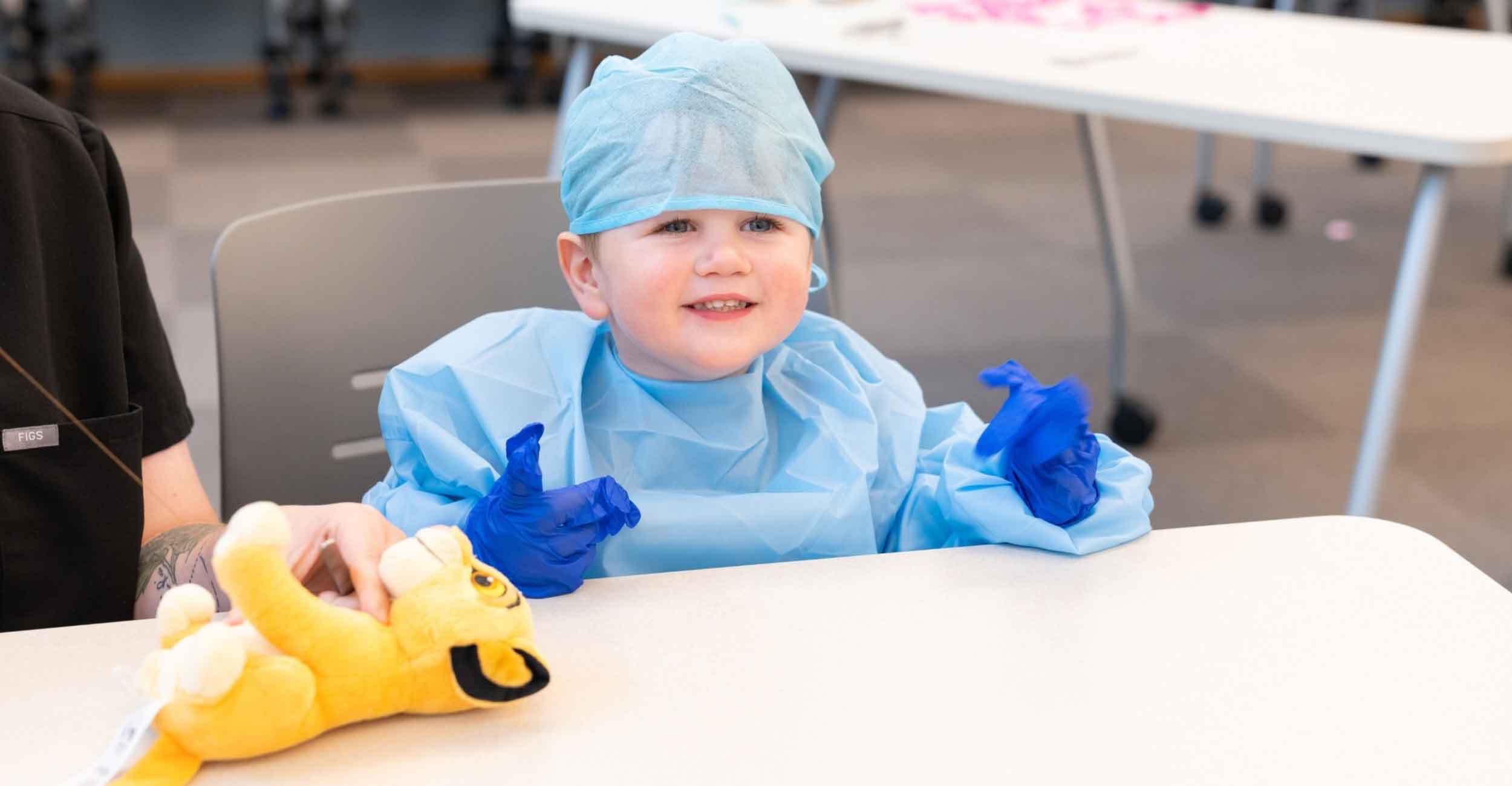 Little boy dressed in surgical gown smiling performing teddy bear surgery.