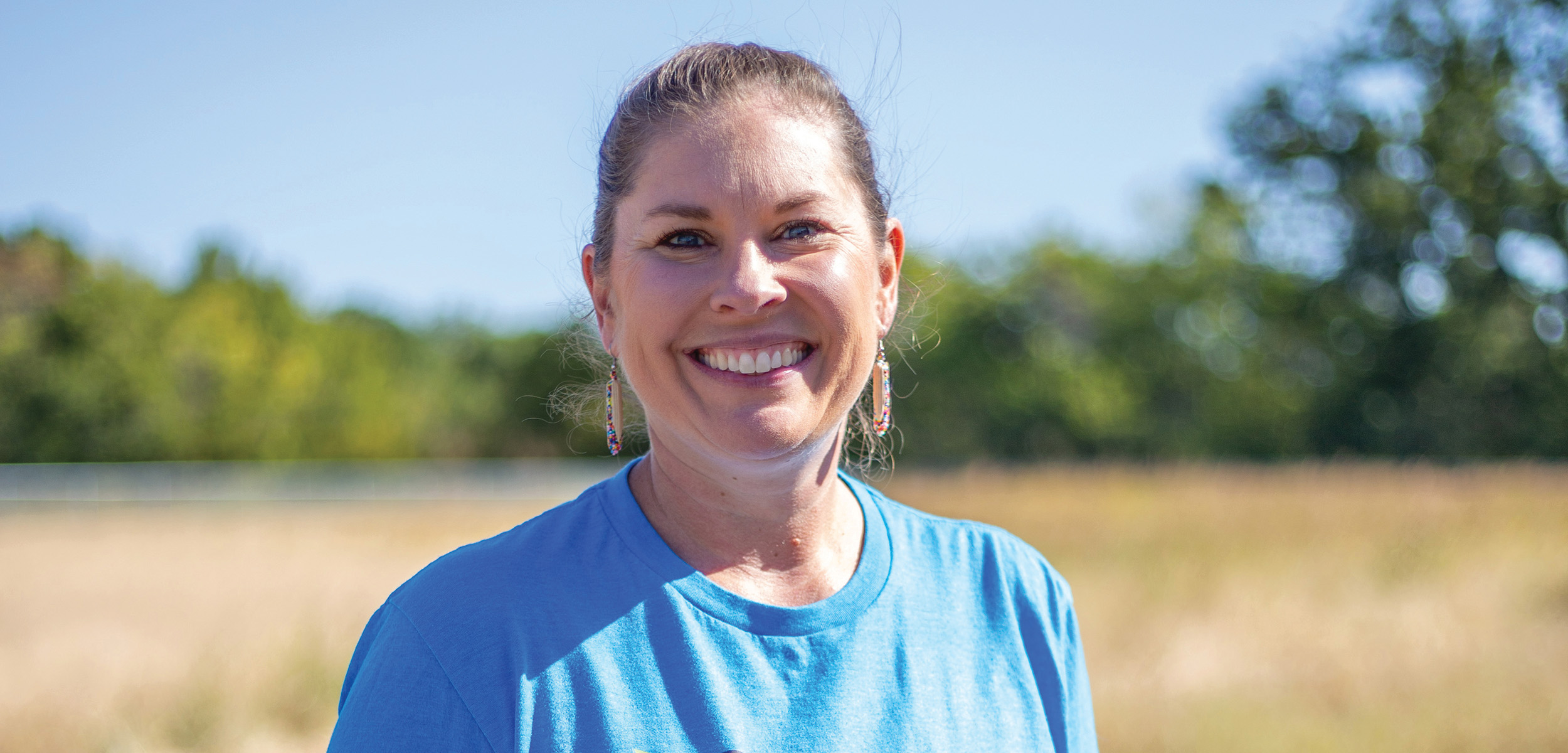 Jann Hayman is standing in a field with a smile on her face.