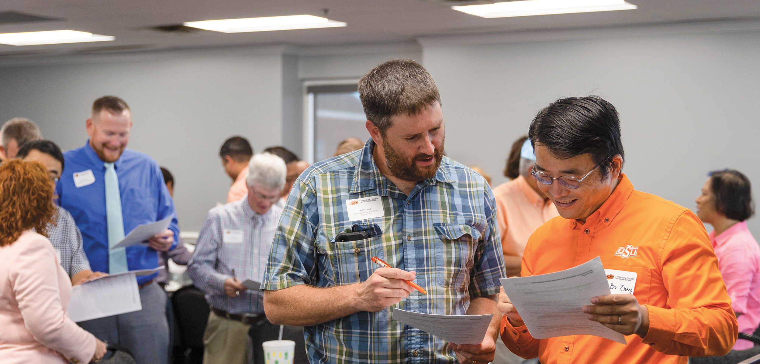 John Long and Bo Zhang are talking over a worksheet at a teaching workshop.