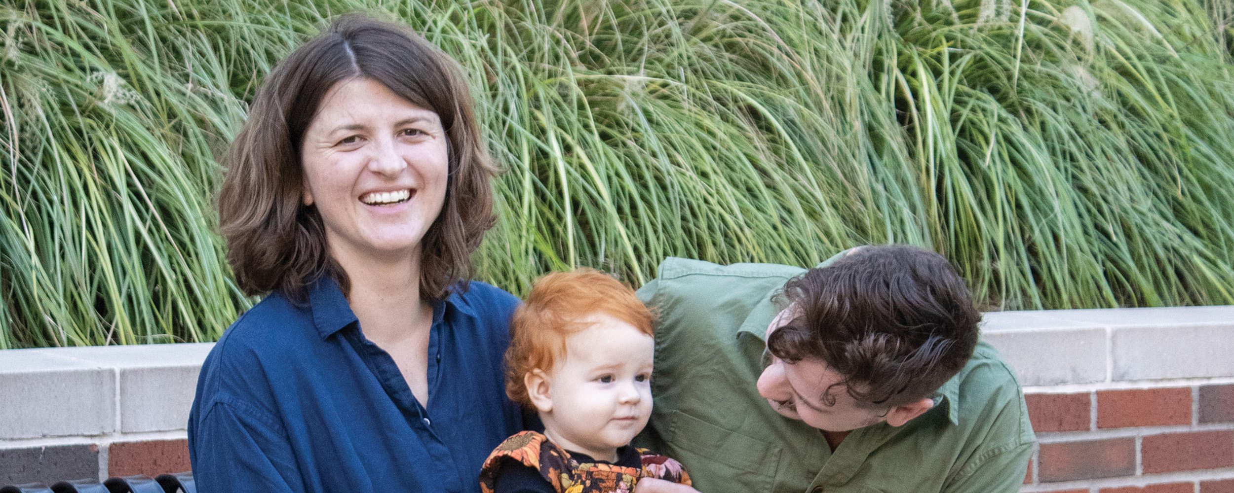 Andrea Jilling and Matthew Bean are sitting on a black bench in front of agricultural hall with their daughter, Ilona.