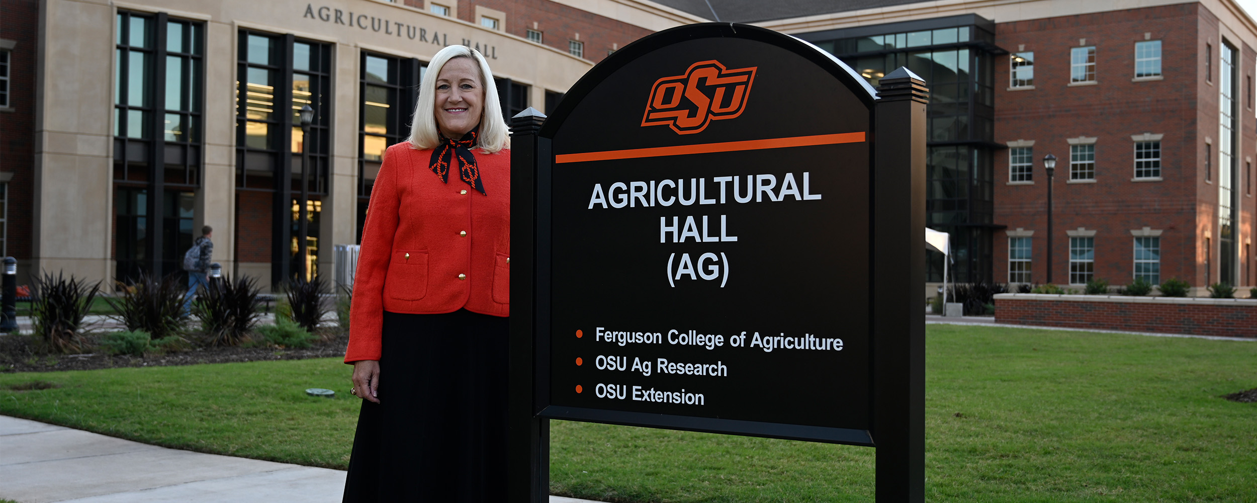 A women standing next to an Agriculture Hall sign in front of Agriculture Hall building on a clear day.