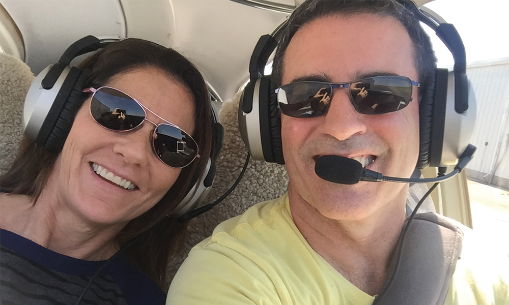 Rhonda and Marc Tower pose together during a helicopter flight with headsets on