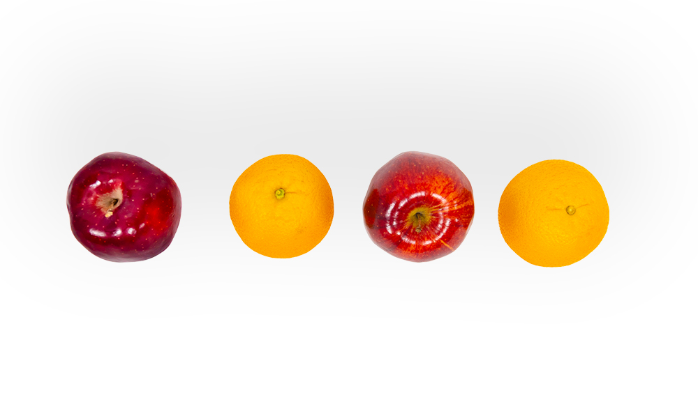 Apples and oranges laid out in a row on a white backdrop.