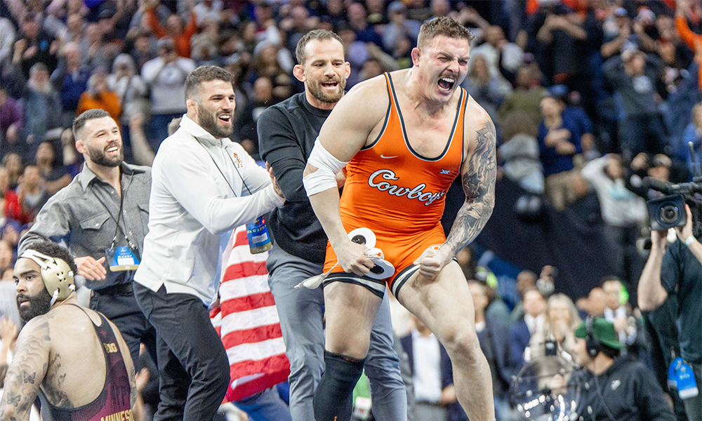 Photo of Wyatt Hendrickson seconds after winning the NCAA Championship. Wyatt is yelling in celebration as his coaches jump for joy and the crows erupts.