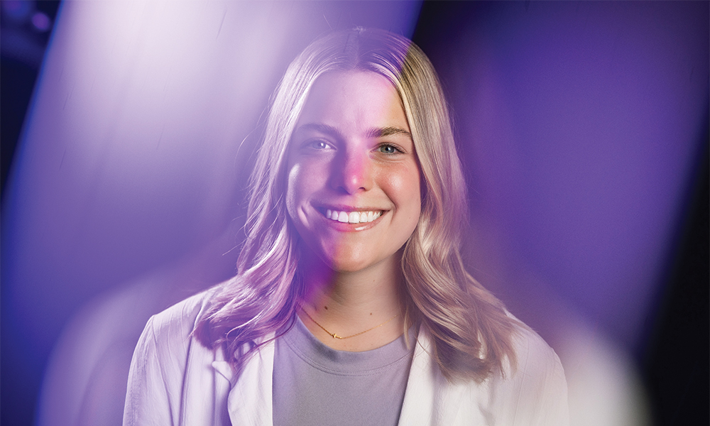 Brooklyn Hawkins, who founded non-profit In the Middle of a Miracle, wearing a white coat and posing in front of a black background with purple light cast on her.