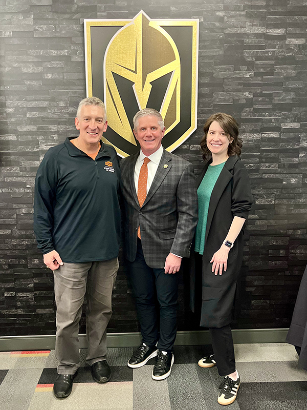 Three individuals pose in front of a Vegas Golden Knights wall decoration.