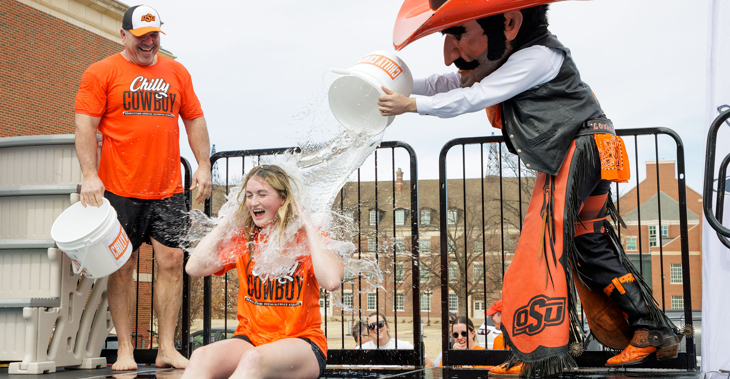 Chilly Cowboy creator Chelsea Fitzgerald gets splashed with a bucket of water by OSU mascot Pistol Pete while First Cowboy Darren Shrum laughs.