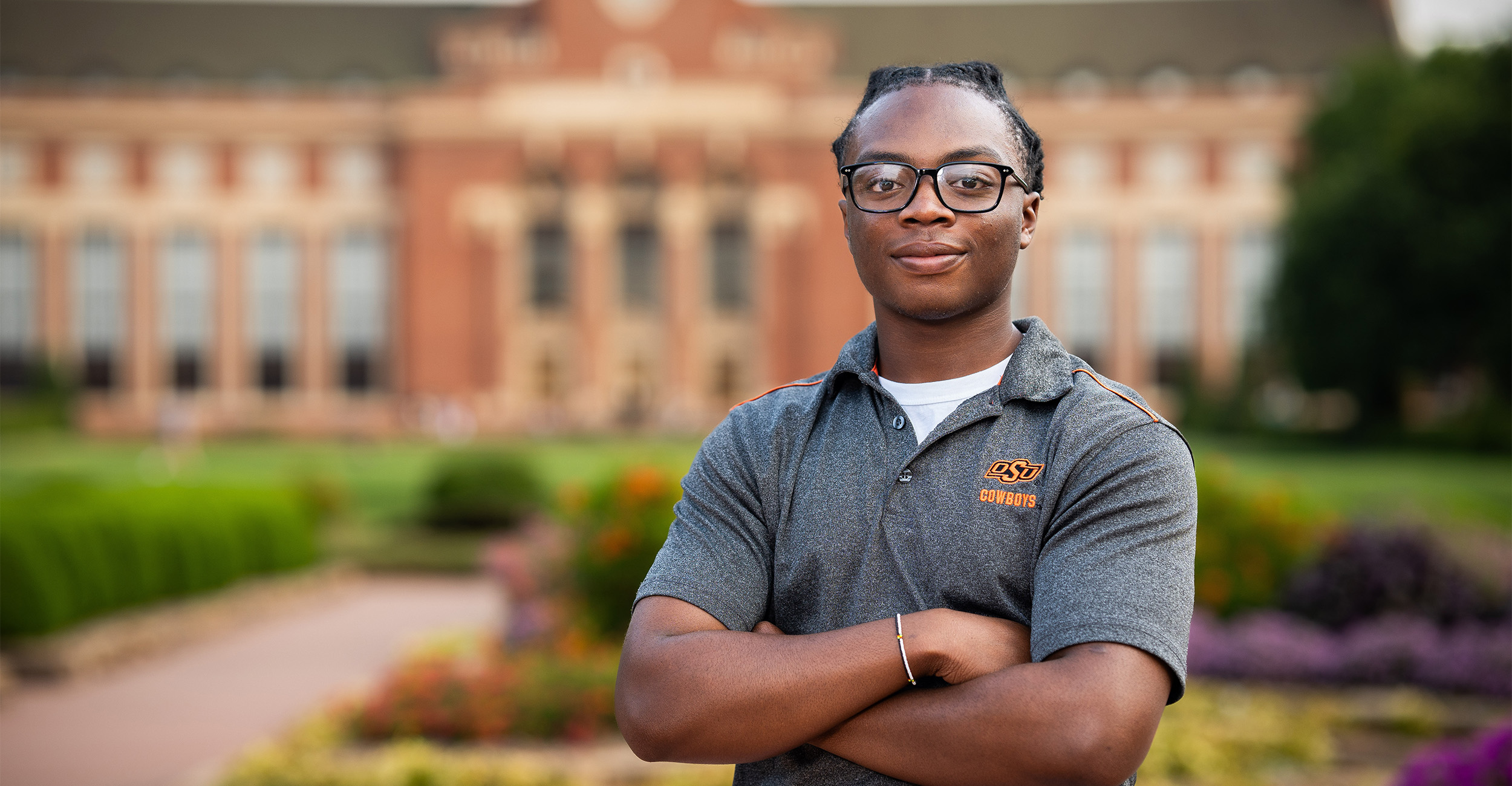 Femi Abioye poses in the formal gardens in the middle of the OSU campus with the Edmon Low Library in the background.