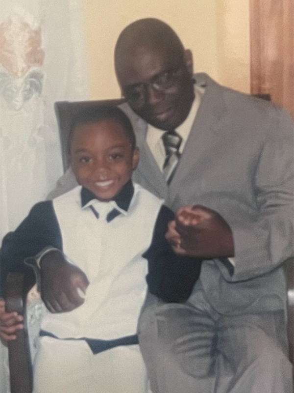 Femi Abioye with his late father Adeolu as a young boy. The two are wearing suits and Femi is sitting in his father's lap.