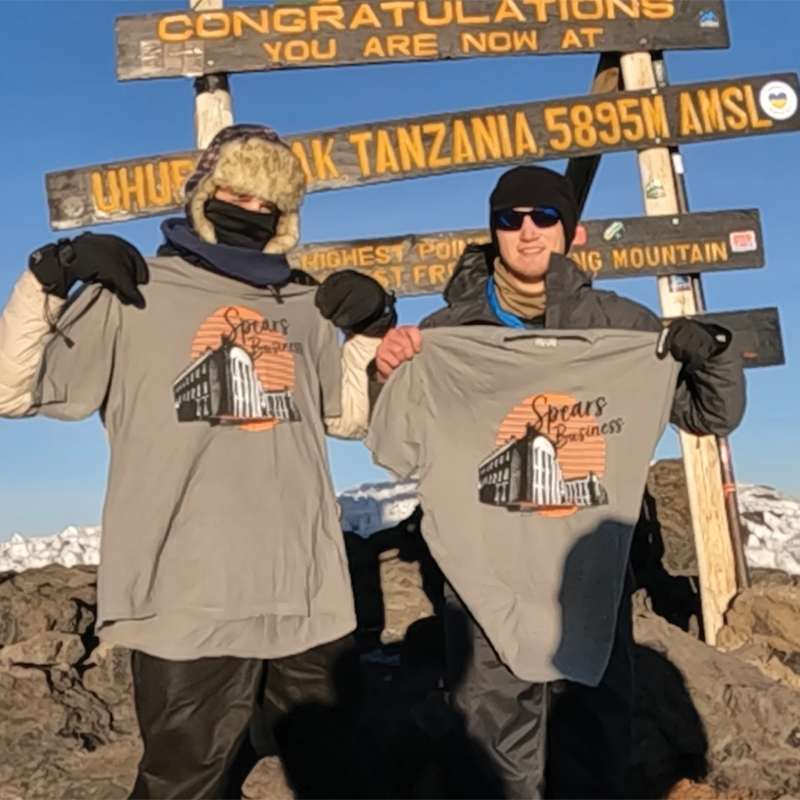 Two men hold Spears Business t-shirts after having just scaled Mt. Kilimanjaro.