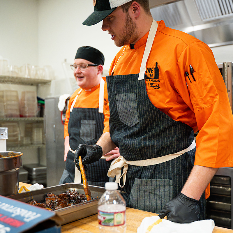 Student chefs in orange clothing and black aprons prepare the Gala meals back stage.