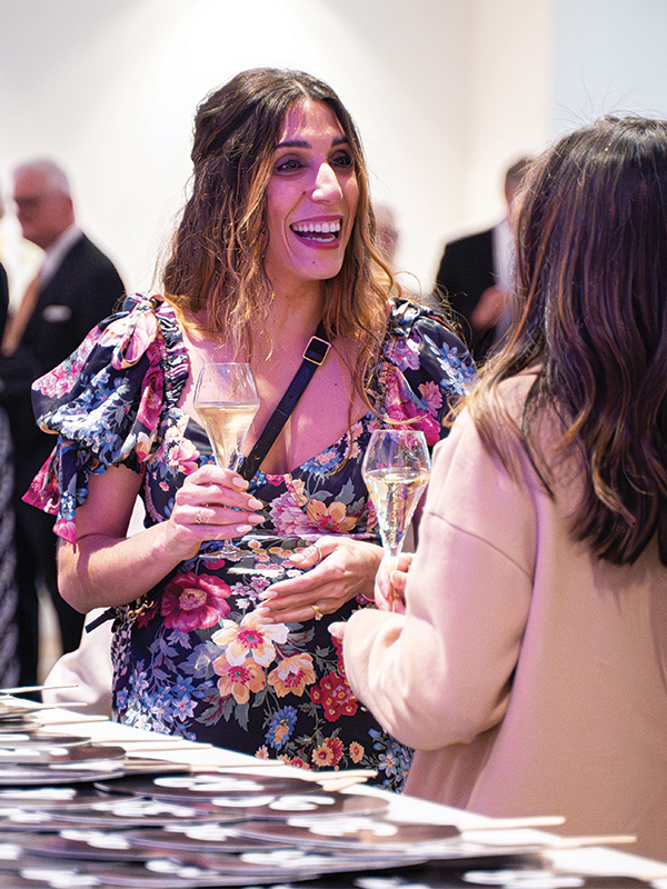 Two female Wine Forum patrons smiling during a conversation while they hold wine glasses.