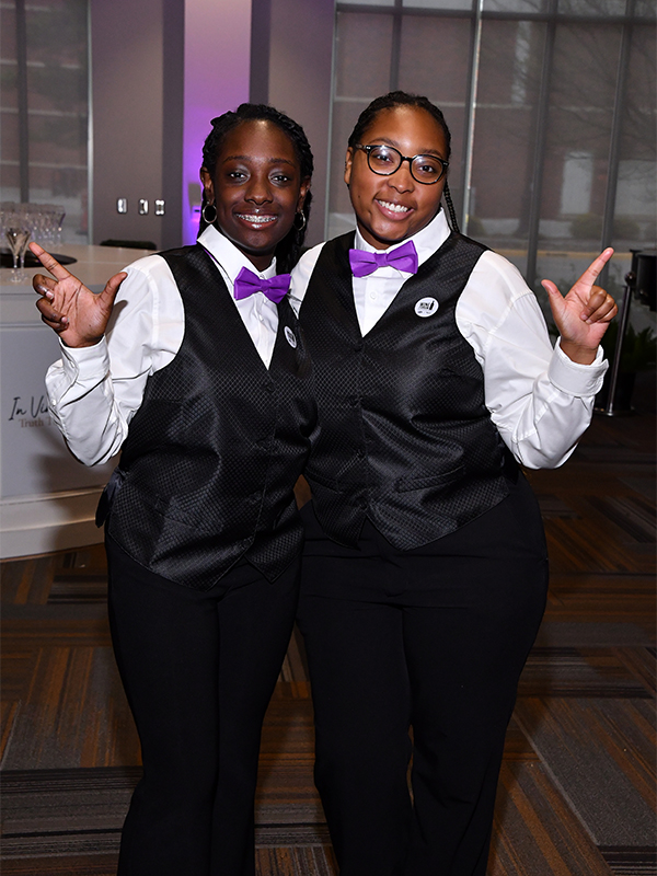 Two students working the Wine Forum Gala smiling and posing together.