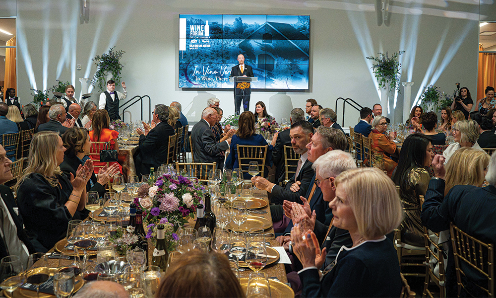 A wide shot from the Wine Forum of Oklahoma that features a room full of people celebrating and an emcee on stage speaking.