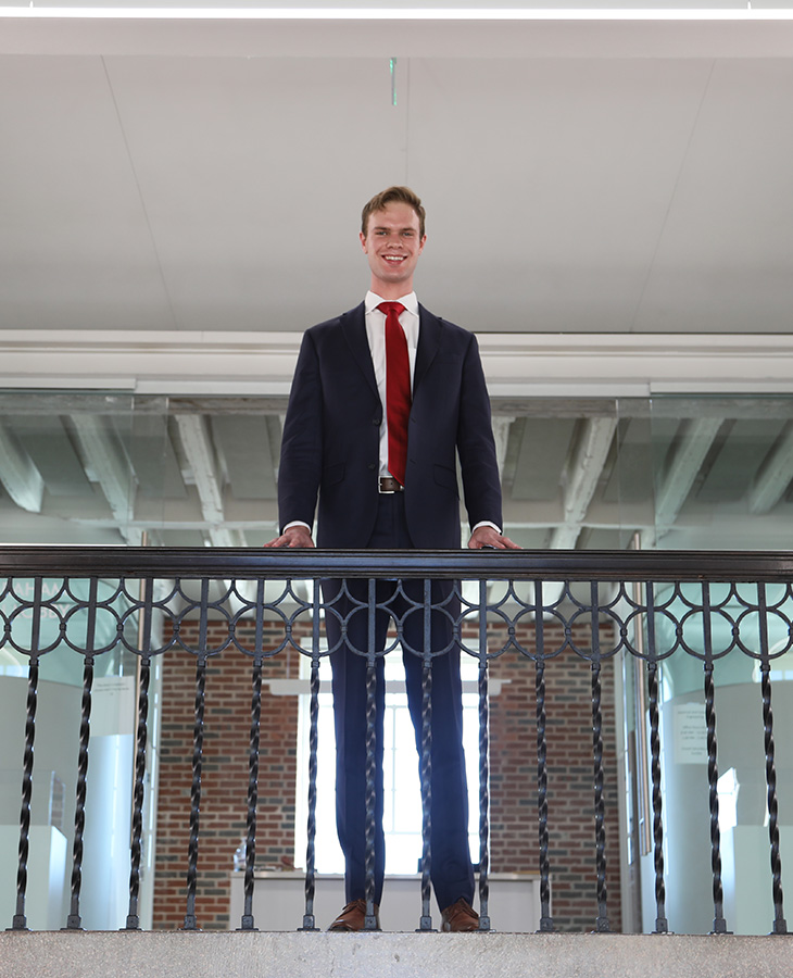 A well-dressed man in a suit and tie poses on a railing, exuding professionalism and elegance in his stance.