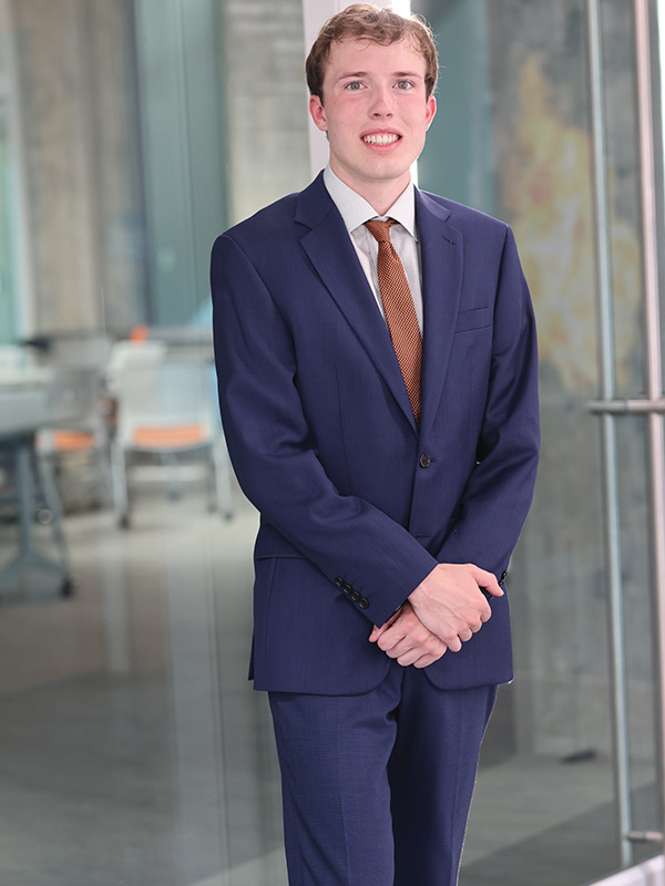 A young man dressed in a suit stands in a modern building.