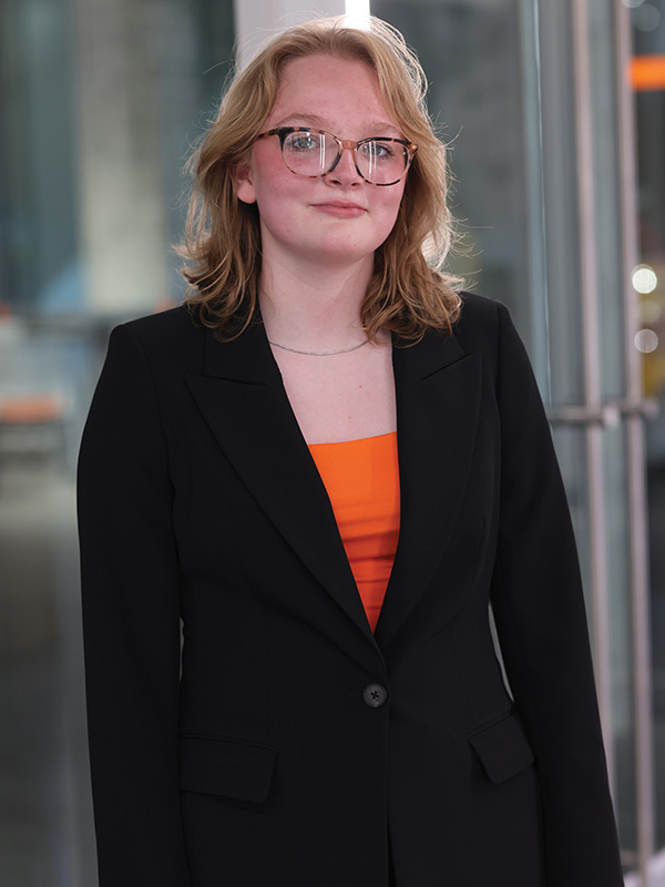 A young woman in professional attire stands in a modern building.