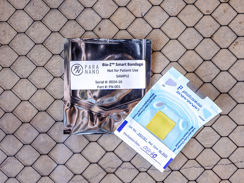 Two packages- one is silver with the words Bio-Z smart bandage. The other package is see through and contains a small yellow square that appears to be made out of a fabric like material.