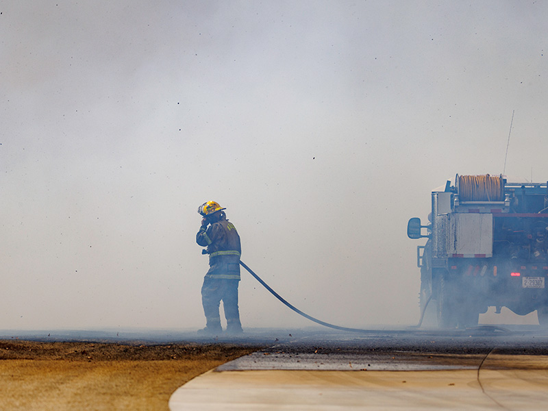 A fireman pulls a firehouse from the firetruck. Smoke enguls the background and foreground.
