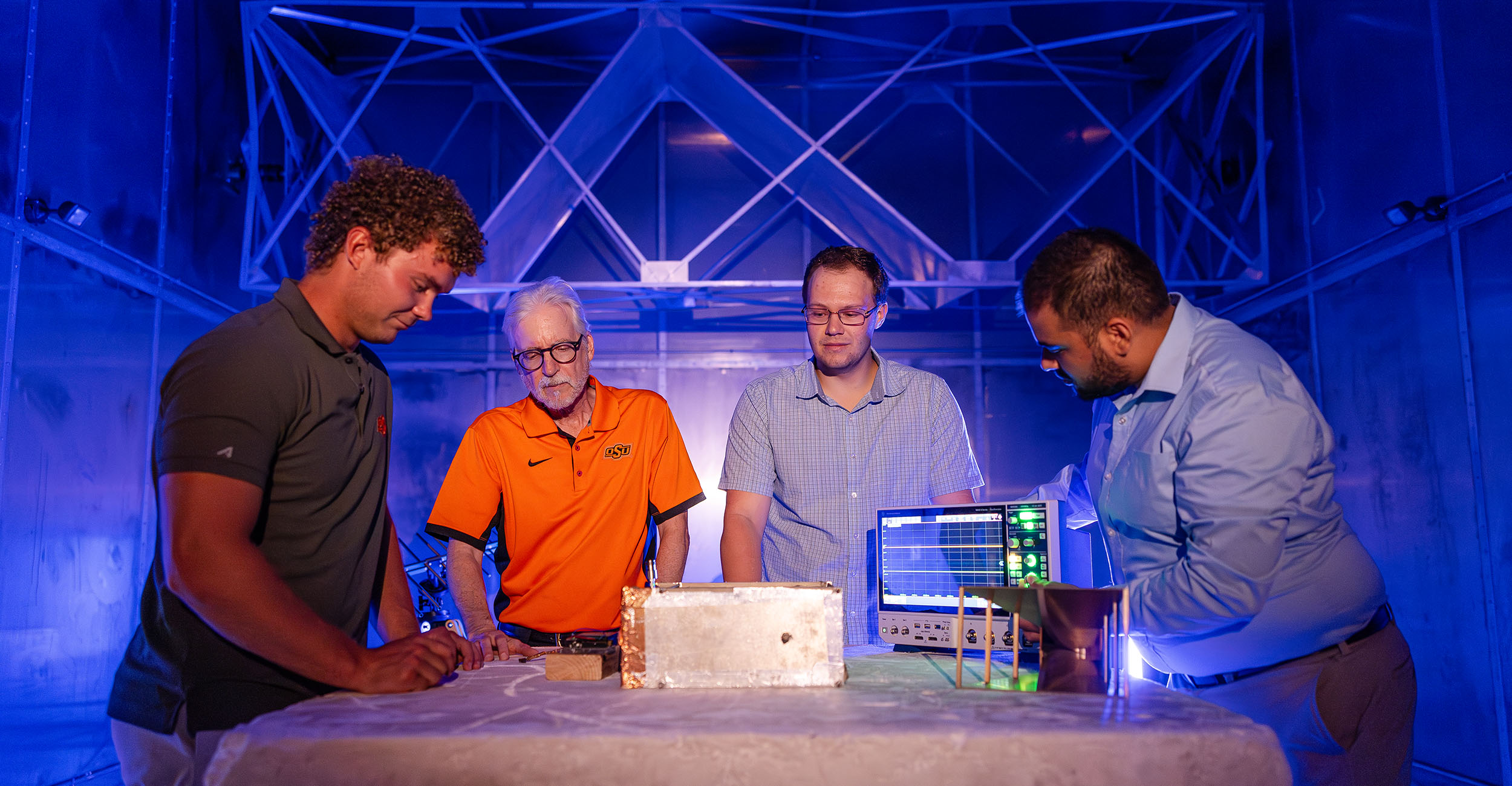 Four people work on scientific equipment inside a room made of all steel.