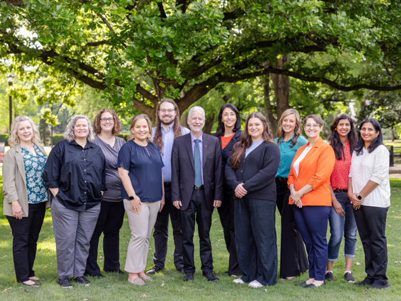 A group photo of 12 people dressed professionaly, standing outside.