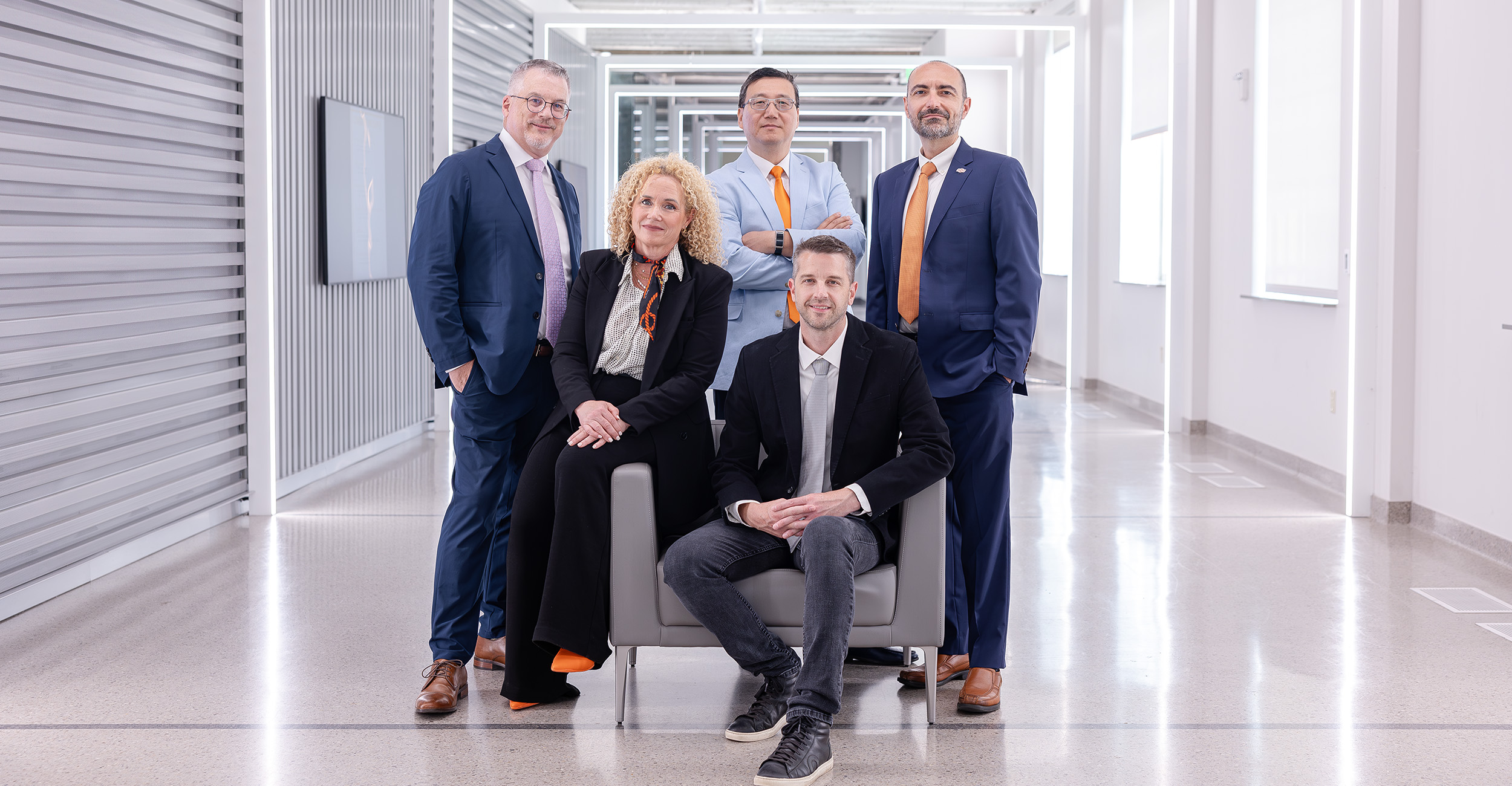 Five professionals dressed in business attire posed together with varying expressions of humble power.