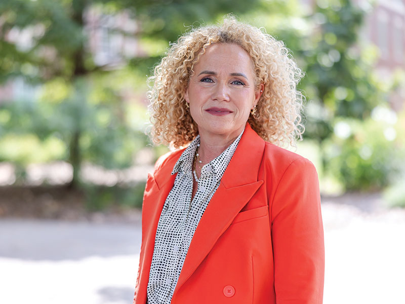 A woman dressed in an orange blazer poses for a headshot outside.
