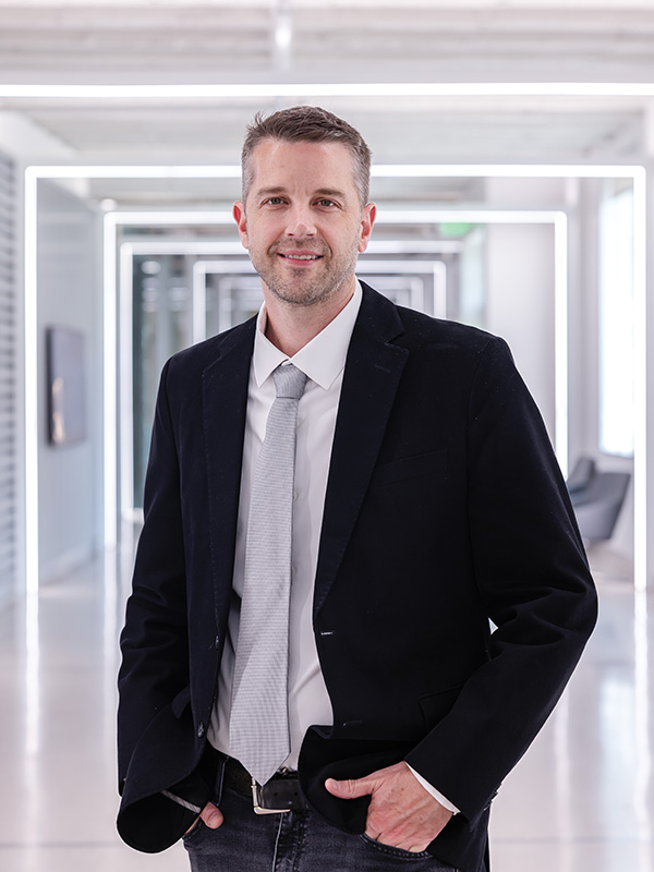 A man in a black suit standing in a modern hallway.