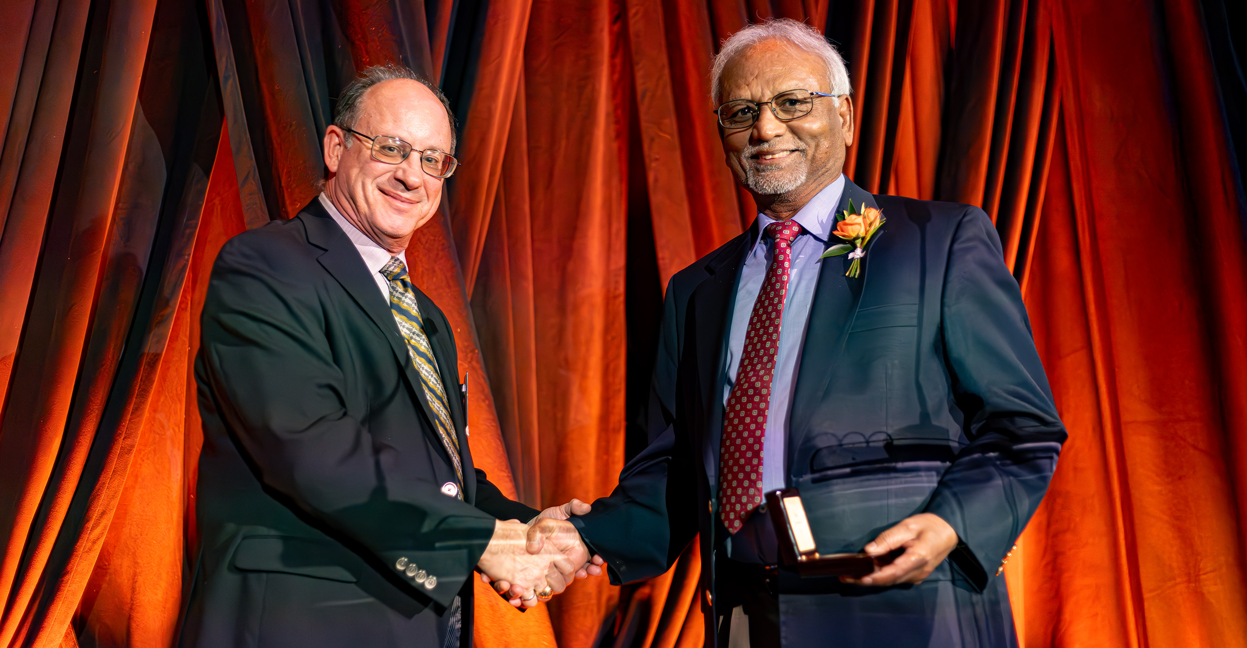 Dr. Rao Surampalli (right) accepts the Lohmann Medal from Dr. Norb Delatte during the 2024 CEAT Hall of Fame and awards banquet. They are shown shaking hands and smiling toward the camera.