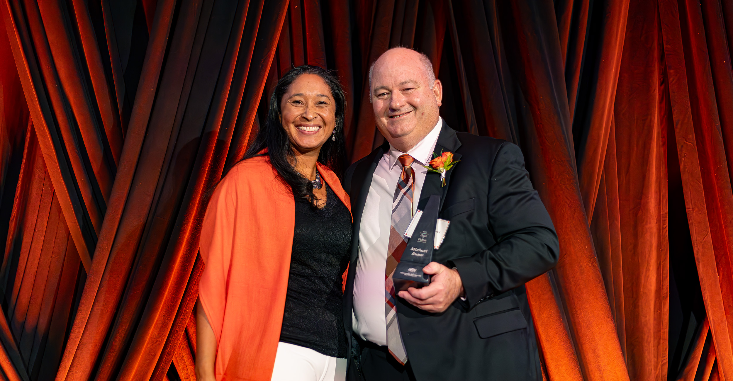 Dr. Mari Chinn and Dr. Michael Buser smile for a photo during the 2024 College of Engineering, Architecture and Technology Hall of Fame banquet. Buser is holding an award that commemorated the occassion.