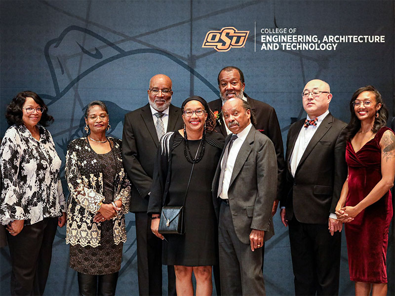 A group of family members poses in front of a black CEAT photo backdrop. All members of the photo are posed and dressed in formal wear.